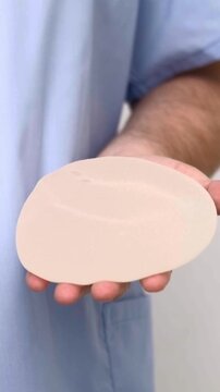 Surgeon holding single silicone breast implant for augmentation surgery, healthcare advertising, plastic surgery, medical equipment.
