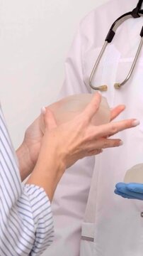 Plastic surgeon holding breast implants during patient consultation in clinic, healthcare marketing, aesthetic surgery, medical advice.