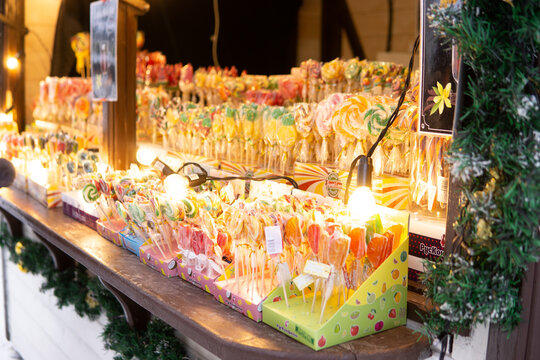 Colorful lollipop display at a festive market stall. Assorted candy and sweet treat selection illuminated by decorative lights for holiday shopping and celebration.