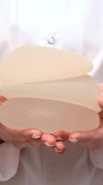Woman holding stack of silicone breast implants in hands, plastic surgery, healthcare, aesthetic medicine, medical care, implant selection.