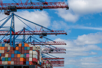 Fototapeta premium Container gantry cranes loading freight boxes on cargo ship at port terminal under blue cloudy sky, global shipping and logistics concept