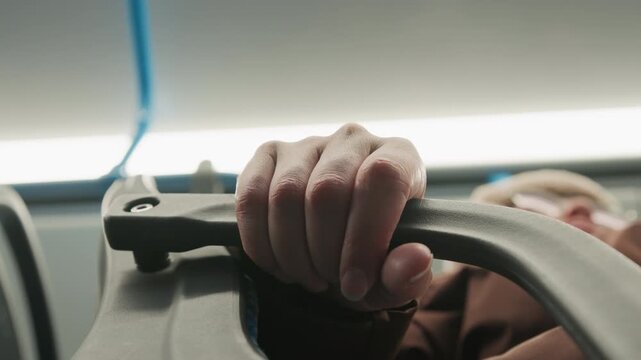 Tight low angle view of passenger hand wrapped around metal overhead rail inside public transport, fingers curled and knuckles pressed firm while vehicle moves through busy city commute