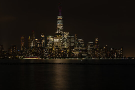An illuminated night view across the water toward downtown Manhattan showcasing brightly lit financial district skyscrapers in New York.
