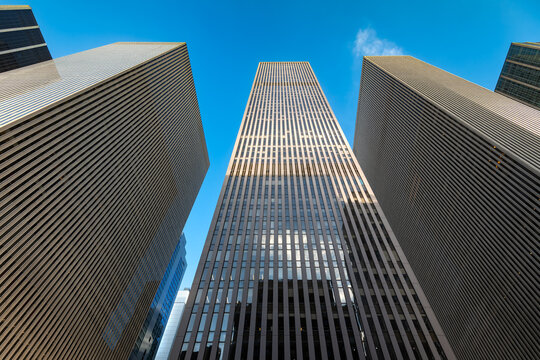 Low angle view looking up at massive corporate office skyscrapers rising high along Avenue of the Americas in New York City.