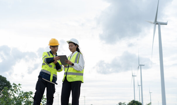 Renewable energy engineers reviewing turbine data on a tablet at a wind farm, representing digital monitoring, asset management, clean power technology and sustainable operations.