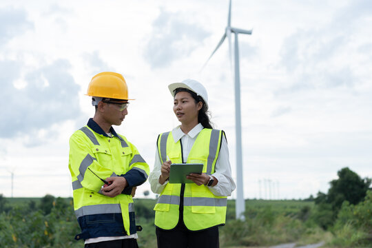 Wind energy engineers discussing turbine operations with a tablet and radio at a renewable power site, representing technical teamwork, inspection, maintenance and sustainable electricity management.
