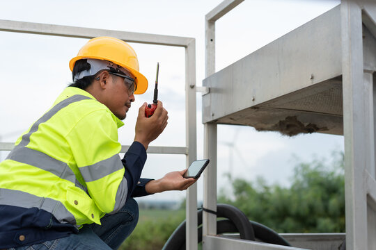 Industrial maintenance technician using smartphone and radio while inspecting mechanical equipment, representing field service, safety communication, diagnostics and preventive maintenance operations.