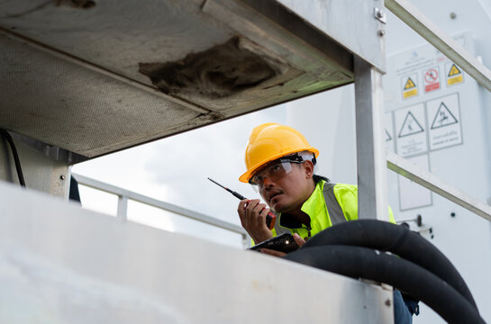 Maintenance technician using radio and smartphone while troubleshooting industrial equipment, representing field diagnostics technical communication, workplace safety and reliable service operations.