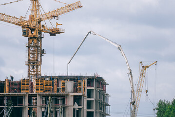 Large apartment block under construction with cranes and concrete pump pouring floors, scaffolding and machinery visible as workers build modern residential infrastructure in cityscape © wifesun