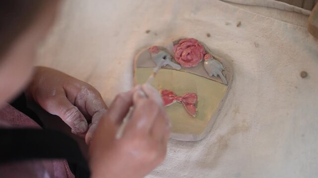 Master class. Children pottery. A view of small children's hands painting a ceramic craft at a table. A girl paints a clay craft using tools, enjoying crafts in a creative workshop. Artistic childhood
