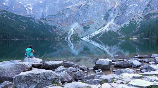 teenager girl with tourist backpack walks along stony shore of lake Eye of Sea (Morskie Oko) in Tatra Mountains, Poland