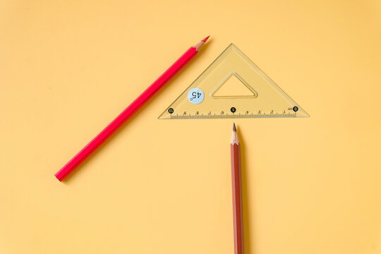 Ruler triangle and color pencils on color background.
