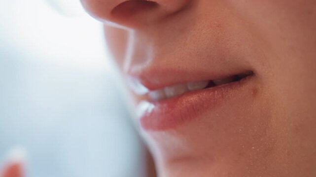 Extreme close view of lower face showing lips, chin, and soft skin detail as person tastes creamy dessert, leaves slight residue on upper lip, and settles into relaxed smile under gentle indoor light