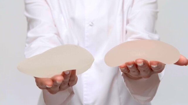 A surgeon showing two silicone breast implants side by side, plastic surgery consultation, medical marketing, aesthetic care.