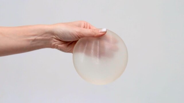 A hand presenting a round silicone breast implant, plastic surgery consultation, medical marketing, aesthetic medicine, healthcare.