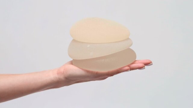 Two stacked silicone breast implants held in a hand, plastic surgery options, medical consultation, healthcare advertising, patient care.