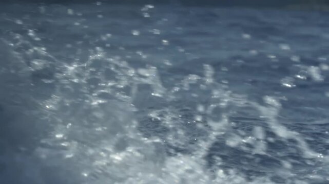 Sailing boat wake splashing on deep blue ocean water