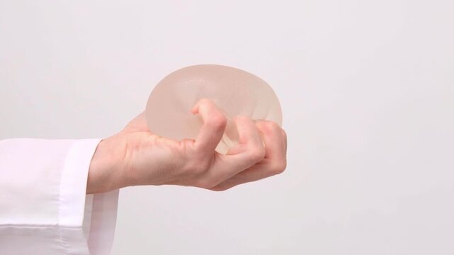 A doctor showcasing a silicone breast implant in a medical clinic, healthcare advertising, plastic surgery, aesthetic medicine consultation.