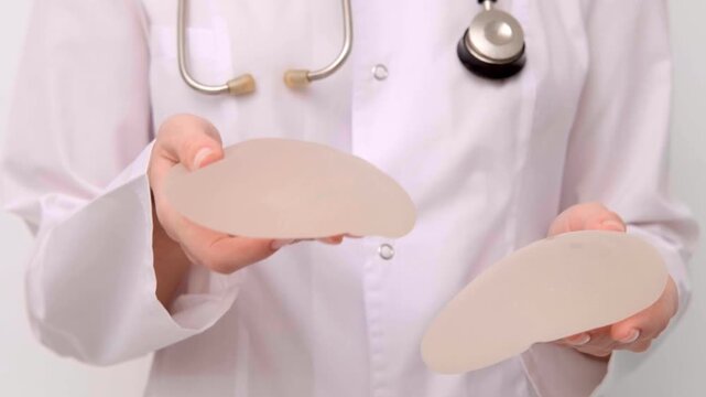 Doctor demonstrating a silicone breast implant texture and flexibility in a medical clinic, healthcare advertising, plastic surgery, consultation.