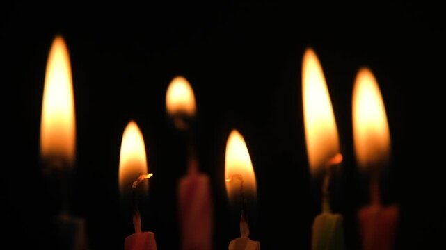Lighting colorful birthday candles with a lighter in the darkness, close-up of candle wicks catching fire and glowing flames creating a warm festive atmosphere during a birthday celebration