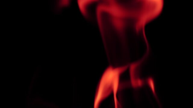 Close-up of red fire flames moving and flickering in darkness. Glowing heat and burning flame texture. Slow motion video.