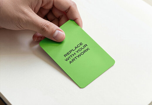 Business card mockup held in hand on white surface, realistic stationery branding presentation with placeholder text, clean office or studio environment, vertical closeup view of paper desk
