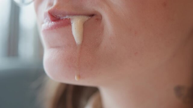 Tight close-up of lower face showing woman brushing lower teeth with foamy toothpaste, paste dripping from lip to chin, conveying active oral care, fresh hygiene, and gentle morning cleaning motion