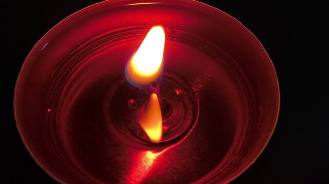Burning tealight candle against dark background, flickering flame creating warm reflections, atmospheric illumination and glowing light for relaxation, meditation, decoration and romantic ambience