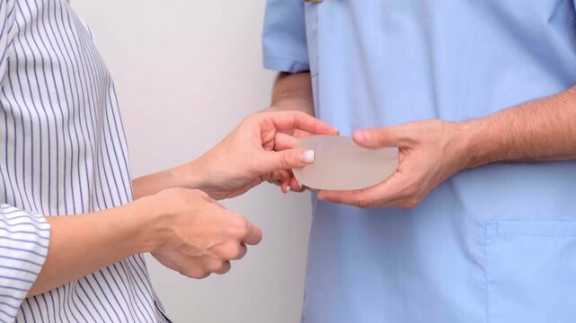 Plastic surgeon showing breast implants to a woman during a medical consultation in a clinic, healthcare advertising, patient care, plastic surgery consultation.