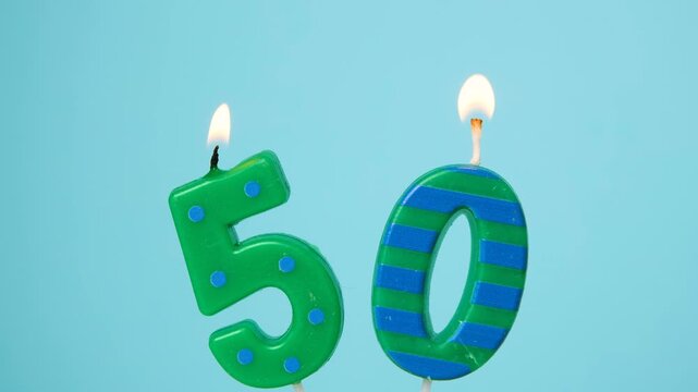 Lighting number fifty birthday candles with a lighter against a bright blue background, close-up of burning flames on decorative numeral candles celebrating a fiftieth birthday, anniversary