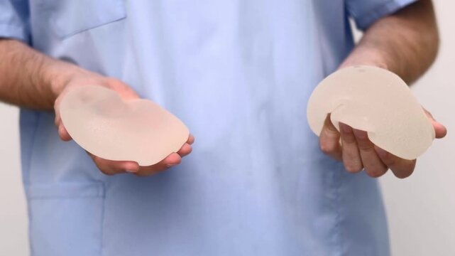 Plastic surgeon in professional scrubs presenting anatomical breast implants, aesthetic medicine and reconstructive surgery clinic, augmentation mammoplasty choice.