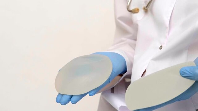 Medical specialist presenting breast implants of varying sizes for aesthetic surgery consultation, plastic surgery clinic, augmentation mammoplasty patient education.