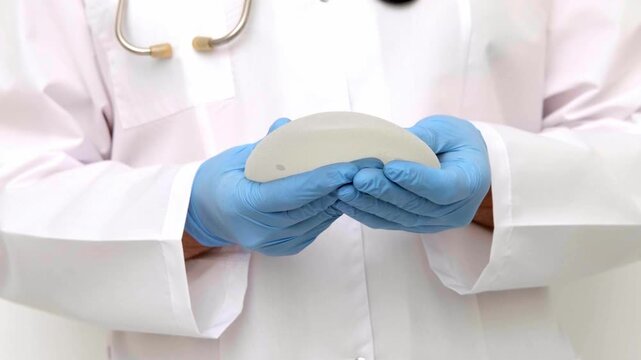 Aesthetic surgeon showcasing breast implant firmness and quality during a medical examination in a clinic, plastic surgery and reconstructive mammoplasty video, patient consultation.