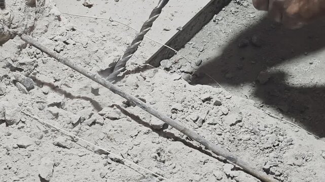 a worker operating a heavy-duty rotary hammer drill on a concrete slab at a construction site, releasing dust and debris near steel rebar. Target audience includes civil engineering firms, industrial