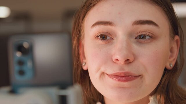 Tight eye-level close-up of young woman interacting with smartphone on mount, progression from focused gaze to gentle smile and relaxed expression indicating pleasant reaction; indoor modern setting