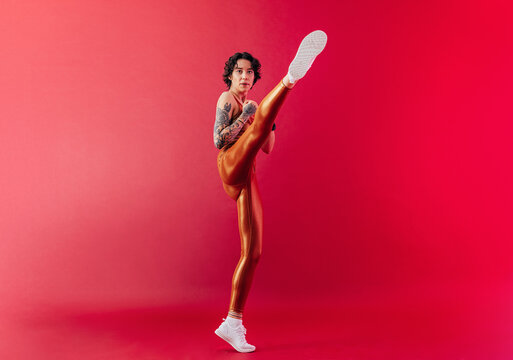 Slim female athlete practicing a leg kick over a crimson background