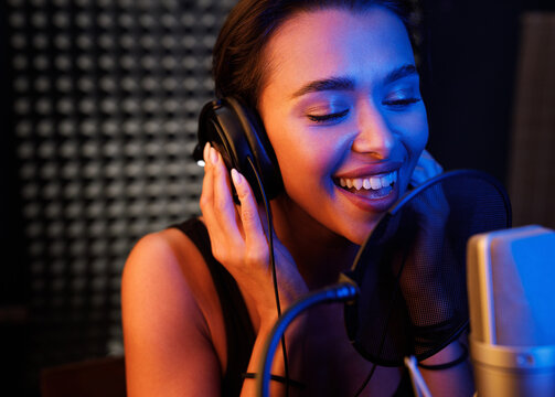 Young smiling female singer performing in a studio under colorful lights