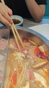 Close up of wooden chopsticks holding raw beef roll into boiling spicy hot pot broth in Ulanqab, Inner Mongolia, China