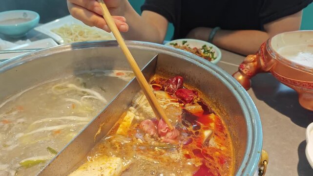 Close up of wooden chopsticks holding raw beef roll into boiling spicy hot pot broth in Ulanqab, Inner Mongolia, China
