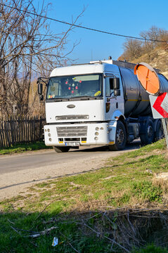 A white Turkish Ford Cargo tanker truck from the 2000s drives along a narrow country road; commercial vehicle and freight transport in rural Kirklareli, Thrace, Turkey 28.03.2025