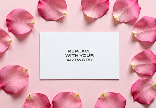 Rectangular card mockup on a pink textured surface with scattered rose petals, flat lay stationery presentation featuring copy space for branding or graphic design, template invitation greeting