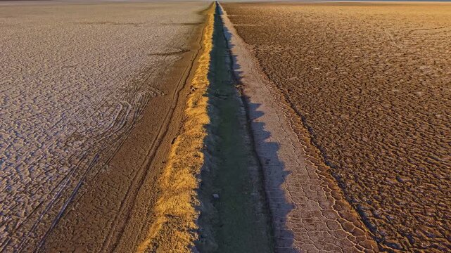 Aerial view of a long ditch cutting through expansive salt flats beneath warm sunset light in Utah
