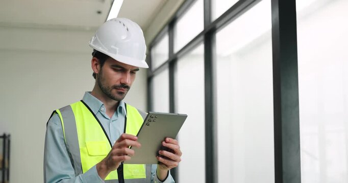 Portrait of Hispanic engineer checks tablet by panotamic windows as holds focused posture. Construction worker taps screen as looks forward during inspection