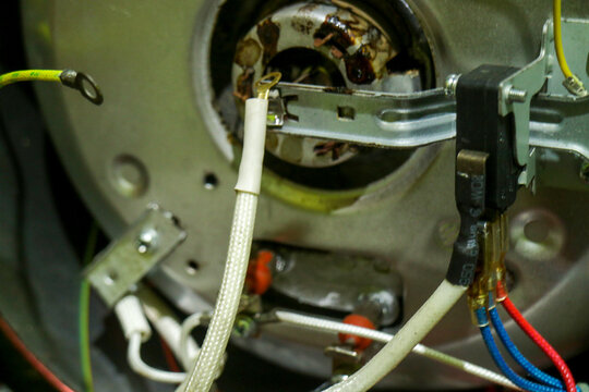 Close-up shows mechanical interior with wires and connectors. Metal housing holds aged, rusted motor component. Cables twist around brackets and terminals in tight space