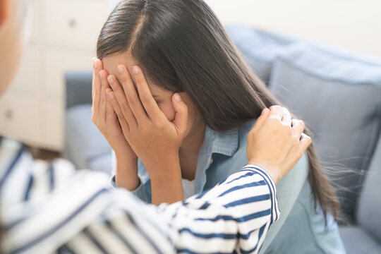 Professional female therapist comforting a depressed sad woman holding hands over her face during a mental health counseling support session on a sofa in the office