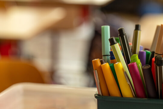 Gros plan sur des crayons color&eacute;s et du mat&eacute;riel scolaire dans un pot, avec une salle de classe lumineuse volontairement floue en arri&egrave;re-plan, concept de rentr&eacute;e et d'&eacute;ducation.