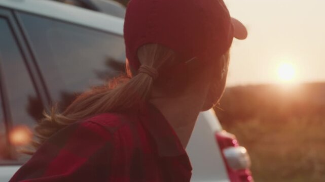 Young woman stands by the big 4x4 off road car and watches sunset in the wild