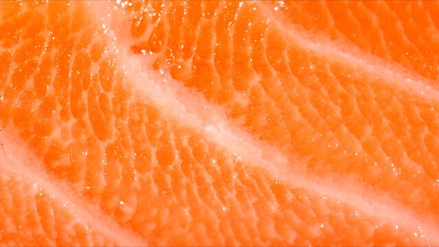 Fresh raw salmon fillet on black plate with macro texture of orange meat and fat marbling stripes.