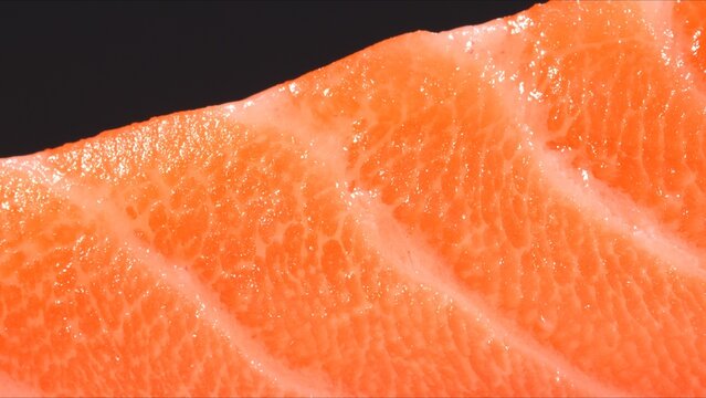 Fresh raw salmon fillet on black plate with macro texture of orange meat and fat marbling stripes.