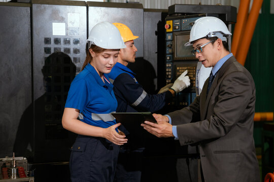 Workers discuss plans in a factory while using tools and equipment during the day